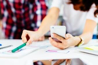 Woman holding a cell phone and comparing information on documents in front of her