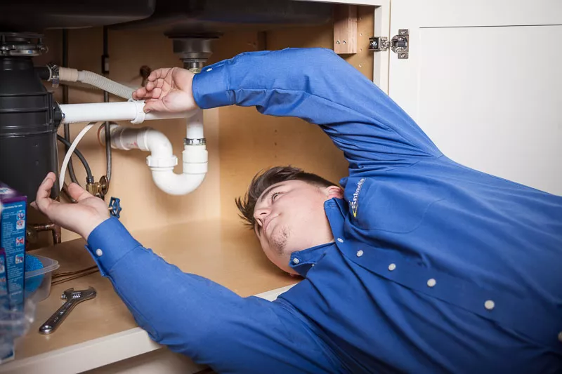 Schneller Knochelmann plumber repairing a pipe below a kitchen sink.