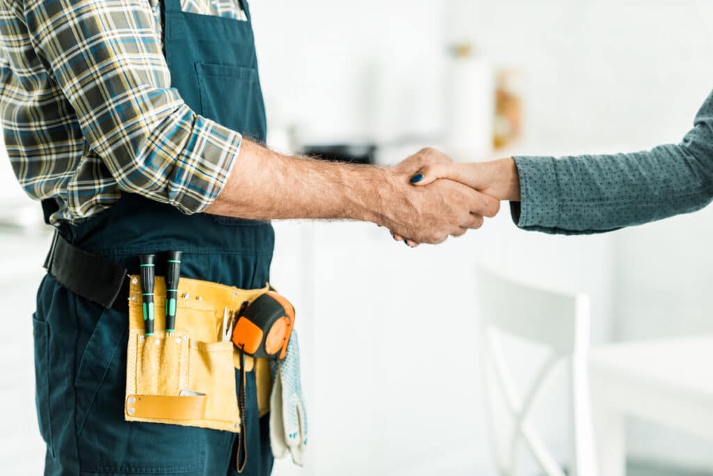 Copped image of plumber and client shaking hands in kitchen.