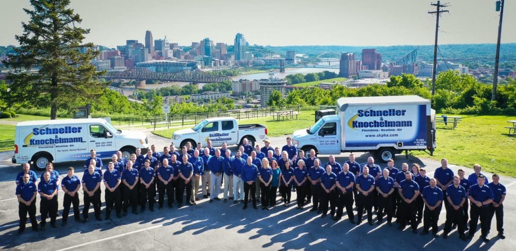 The Schneller Knochelmann team standing in front of service vehicles with a city skyline in the background