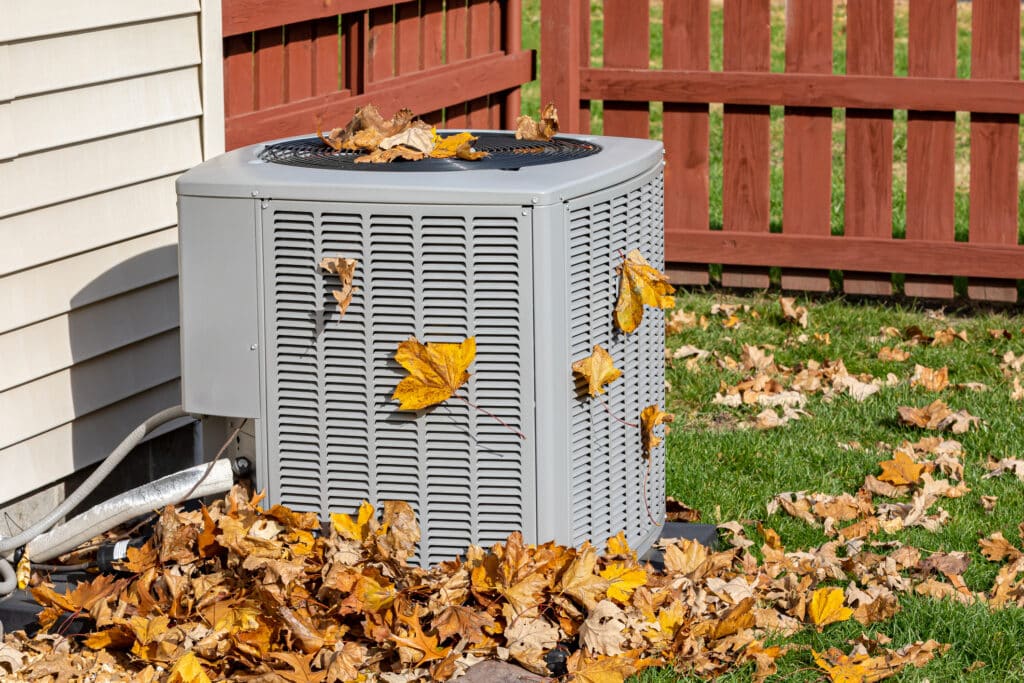 Outdoor AC unit covered with brown and orange leaves.