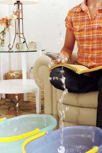 Woman sitting on couch, two large buckets in front of her are collecting water from a leak