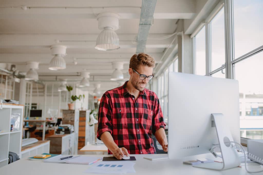 Shot of happy young man working on desktop computer in modern workplace